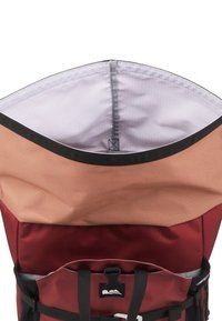 Vue de dessus d'un sac à dos rouge et beige ouvert montrant un intérieur blanc spacieux avec une bordure noire et une fermeture à boucle noire.