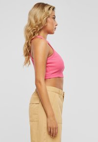 Strammet rosa ribbestrikket crop top med brede stropper, kombinert med beige cargo bukser med sidelommer og en avslappet silhuett.