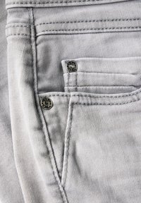 Denim gris délavé avec deux boutons argentés, couture visible et un détail de poche près du coin supérieur gauche. Texture douce et finition lisse.