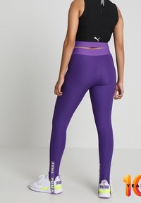 Lila ribbade leggings med hög midja och kontrasterande lavendelfärgad kant, med "PUMA"-logotyp på nederkanten av benen. Bärs med vita sneakers.