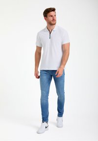 Hvid polo shirt med lynlås krave, struktureret stof, parret med lyseblå jeans og hvide sneakers med sorte detaljer.
