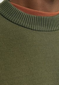 Suéter de punto con un cuello acanalado verde y un interior de color óxido en contraste. Tejido texturizado con un grosor uniforme.