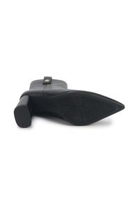 Bottine en cuir noir avec talon carré, pointe effilée, sangle décorative avec bouton doré et semelle en caoutchouc à motifs vue de dessous.