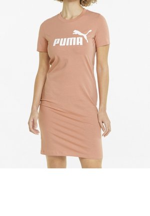 Femme portant une robe à manches courtes couleur pêche avec un logo Puma blanc sur la poitrine, debout devant un fond blanc uni.