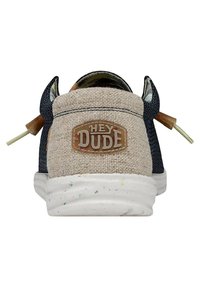 Scarpa slip-on in canvas con un retro beige testurizzato, lati blu scuro e il logo "HEY DUDE". Presenta una suola colorata a macchie e lacci decorativi.
