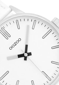 Montre-bracelet en argent avec un cadran blanc. Les caractéristiques incluent des index horaires noirs, des aiguilles argentées et un logo de marque "oozoo" bien visible au centre.