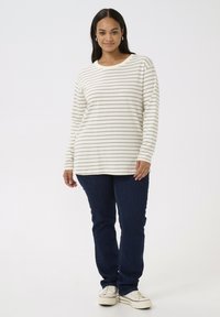 Long-sleeve, cream top with horizontal light brown stripes, paired with dark blue jeans and white sneakers. Simple neckline and relaxed fit.
