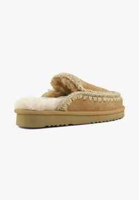 Sandfarvet ruskindstøffel med pelsfor, detaljer med flettet kant, flad sål og rundet tådesign. Velegnet til indendørs brug.