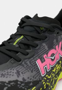 Svart löparskon med en texturerad syntetisk ovandel och rosa "HOKA"-logotyp, svarta snören och en flerfärgad mellansula med ett mönstrat mönster.