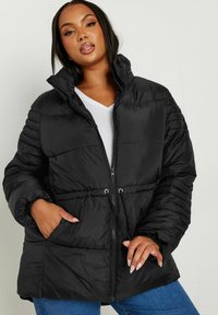 Svart puffjacka med dragkedja fram, hög krage och elastiska ärmslut. Har dragsko i midjan, två sidofickor och kviltad textur.