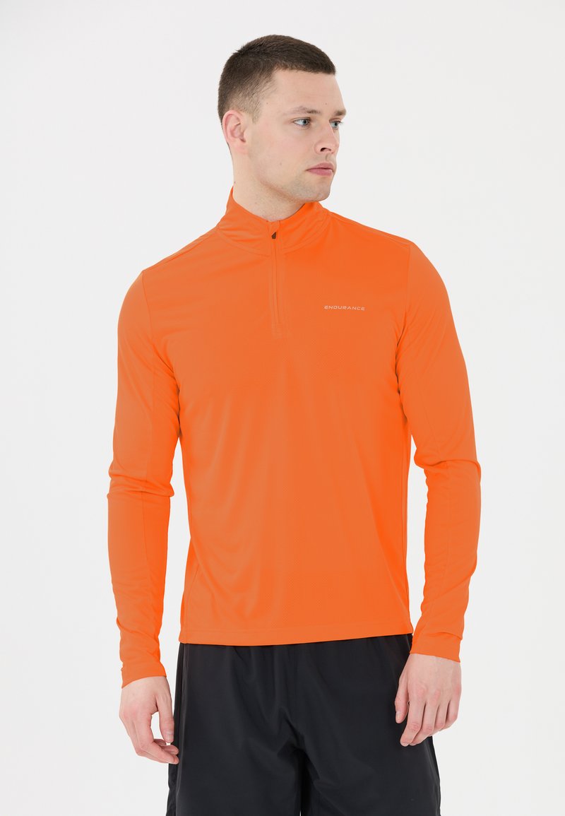 Oranssi pitkähihainen urheilupaita, jossa on neljänneksen vetoketju kauluksessa, valmistettu kevyestä teksturoidusta kankaasta. Rinnassa logo.