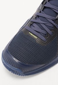 Chaussure de sport bleu marine en tissu respirant, semelle en caoutchouc et accents noirs contrastés. Présente des surfaces texturées et un détail de logo.