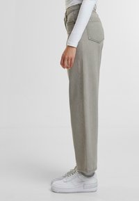 Jeans de talle alto en gris claro con un corte recto, bolsillos frontales y una textura suave, combinados con zapatillas blancas.