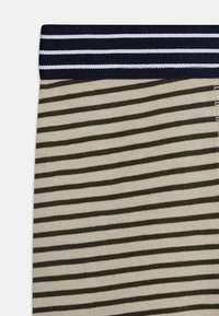 Stripet stoff med en beige bakgrunn og mørkegrønne horisontale linjer. Livremmen er marineblå med hvite striper, noe som indikerer elastisk materiale.