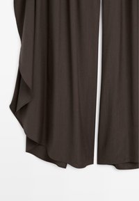 Pantalon large marron foncé avec ourlet fluide, montrant la texture du tissu et un détail drapé sur le côté, sur un fond uni.