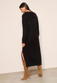 Rochie tricotată neagră cu mâneci lungi și o deschidere pe lateral, asociată cu cizme din suede bej, până la genunchi. Textură netedă, design simplu, până la genunchi.