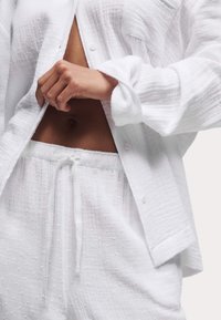 Chemise blanche texturée et pantalon assorti, avec fermeture à boutons et taille élastique. Le tissu présente un motif à pois subtil.