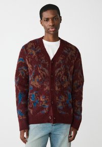 Cardigan en tricot bordeaux présentant un motif texturé avec des accents marron et bleu, cinq boutons et un design en col en V.