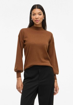 Pull en tricot marron avec un col montant, des manches longues bouffantes et une texture lisse, associé à un pantalon noir. Design simple, sans motifs visibles.