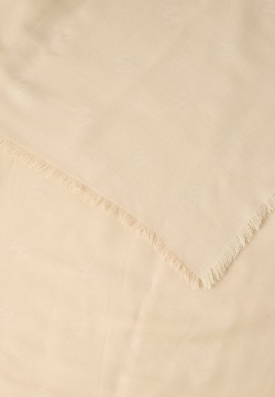 Ανοιχτό μπεζ ύφασμα με διακριτικά υφαντά σχέδια και απαλά κρόσσια στις άκρες, διπλωμένο διαγώνια πάνω σε μια λεία μπεζ επιφάνεια.