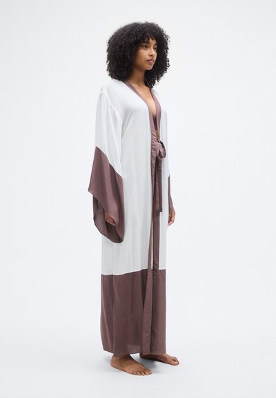 Μακρύ ρόμπα σε στυλ κιμονό σε λευκό και μαβί, με φαρδιά μανίκια, ζώνη στη μέση και ελαφρύ, αέρινο ύφασμα.