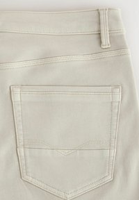 Nahaufnahme von hellbeigem Denimstoff, der eine Gesäßtasche mit doppelt genähten Nähten und eine Gürtelschlaufe am Bund zeigt.