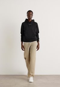 Sudadera negra con cordones, pantalones de pierna ancha color crema y zapatillas blancas. Diseño simple y limpio con una textura suave y colores neutros.