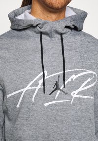 Felpa grigia realizzata in tessuto morbido con cappuccio regolabile. Presenta un grande logo bianco scritto "AIR" e una silhouette nera di una figura che salta.