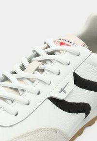 Λευκό δερμάτινο αθλητικό παπούτσι με μαύρες σουέντ λεπτομέρειες, υφασμένο κάλυμμα μύτης και γκρι κορδόνια. Διαθέτει ετικέτα με λογότυπο και καρδιές στη γλώσσα του παπουτσιού.