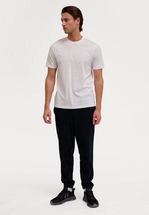White cotton t-shirt with short sleeves, round neckline, and small logo; paired with black sweatpants and black athletic shoes.