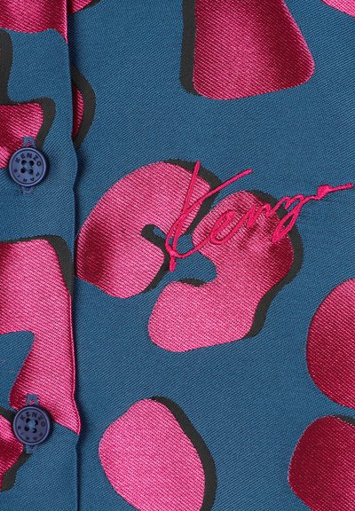 Getextureerde blauwe stof met grote roze abstracte patronen, voorzien van een donkeromlijning. Inclusief een blauwe knoop en een roze geborduurde merknaam.