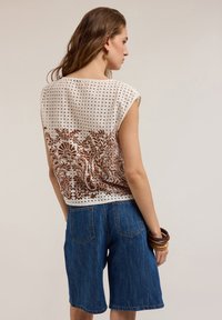 Top bianco a maniche corte con tessuto perforato e stampa floreale marrone sul retro, abbinato a pantaloni corti in denim blu.