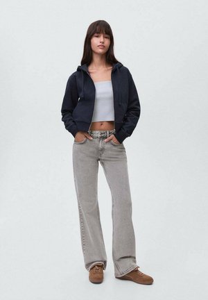 Felpa crop navy con tasche frontali, abbinata a jeans a gamba larga grigio chiaro e sneakers marroni. Tessuto morbido e vestibilità rilassata.