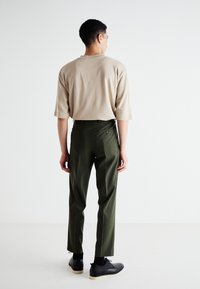 Chemise beige à manches courtes, pantalon vert ajusté avec poches arrière et coupe droite, porté avec des chaussures noires, vu de dos.