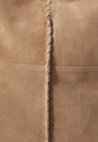 Matière en suède tan avec une texture lisse. Présente un détail de couture tressée courant verticalement et un minimum de coutures le long des bords.