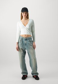 Crop top blanc à manches longues en rib, avec un décolleté en V profond, associé à un jean baggy en denim bleu clair et des baskets noires avec des accents roses.