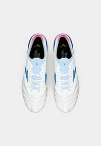 White football shoes with light blue accents, featuring a textured upper, pink heel trim, blue side stripes, and flat white laces.