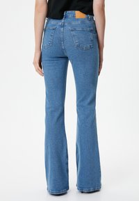 Jeans acampanados de mezclilla azul ajustados con cintura alta, que cuentan con bolsillos traseros y un parche de cuero marrón en la cintura.