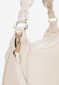Krémová kožená kabelka s texturovaným povrchem, zlatými doplňky a polstrovaným ramenním popruhem s klipsovým uchycením.