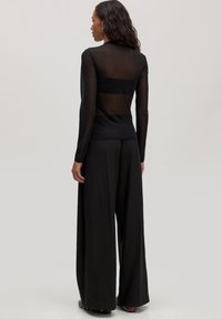 Zwarte top met lange mouwen en een doorzichtige achterkant, gecombineerd met zwarte wijde broek. De top heeft een soepele textuur en een aansluitend ontwerp.