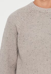 Maglione grigio a maglia con un motivo testurizzato e a coste. Presenta un scollo rotondo e maniche raglan. Realizzato in un materiale morbido e spesso.