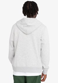 Šedá bavlnená mikina s džersejovou textúrou, nastaviteľnou kapucňou a rebrovanými manžetami. Má voľný strih a prednú vrecko.