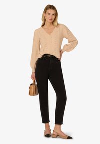 Kremowy sweter dzianinowy z falbaniastym dekoltem i detalami w liście, zestawiony z czarnymi dżinsami z wysokim stanem i beżowymi butami na słupku.