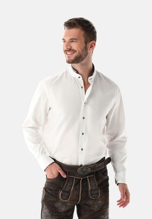 Weißes Hemd mit Stehkragen und braunen Knöpfen. Getragen zu dunklen Lederhosen, die mit aufwendigen floralen Mustern verziert sind.