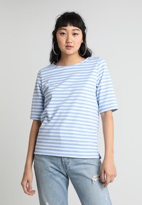 Lyseblå stribet T-shirt i blødt bomuldsstof, med bred udskæring og korte ærmer. Sammen med slidte lyse denimjeans.