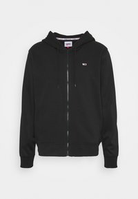 Felpa nera con zip e cappuccio, con cordini, piccolo logo di Tommy Jeans sul lato sinistro del petto, polsini a coste e cappuccio.