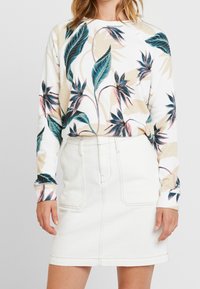 Sudadera blanca de manga larga con estampado botánico en azul y rosa; combinada con una falda de mezclilla blanca de talle alto, hasta la rodilla, con bolsillos.