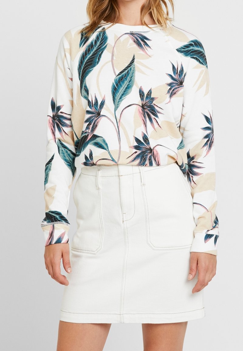 Sudadera blanca de manga larga con estampado botánico en azul y rosa; combinada con una falda de mezclilla blanca de talle alto, hasta la rodilla, con bolsillos.