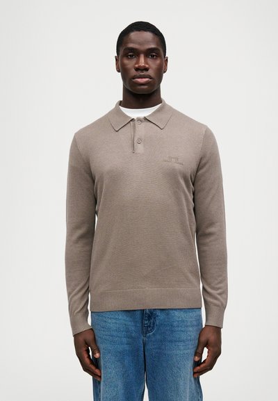 Camisa polo de manga larga marrón con cuello, con una tela texturizada y un logo sutil en el pecho, combinada con vaqueros de mezclilla azules.