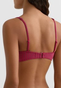 Różowy biustonosz z fakturowanym wzorem, regulowanymi ramiączkami oraz zapięciem na haftki z tyłu. Materiał wydaje się gładki i dopasowany.